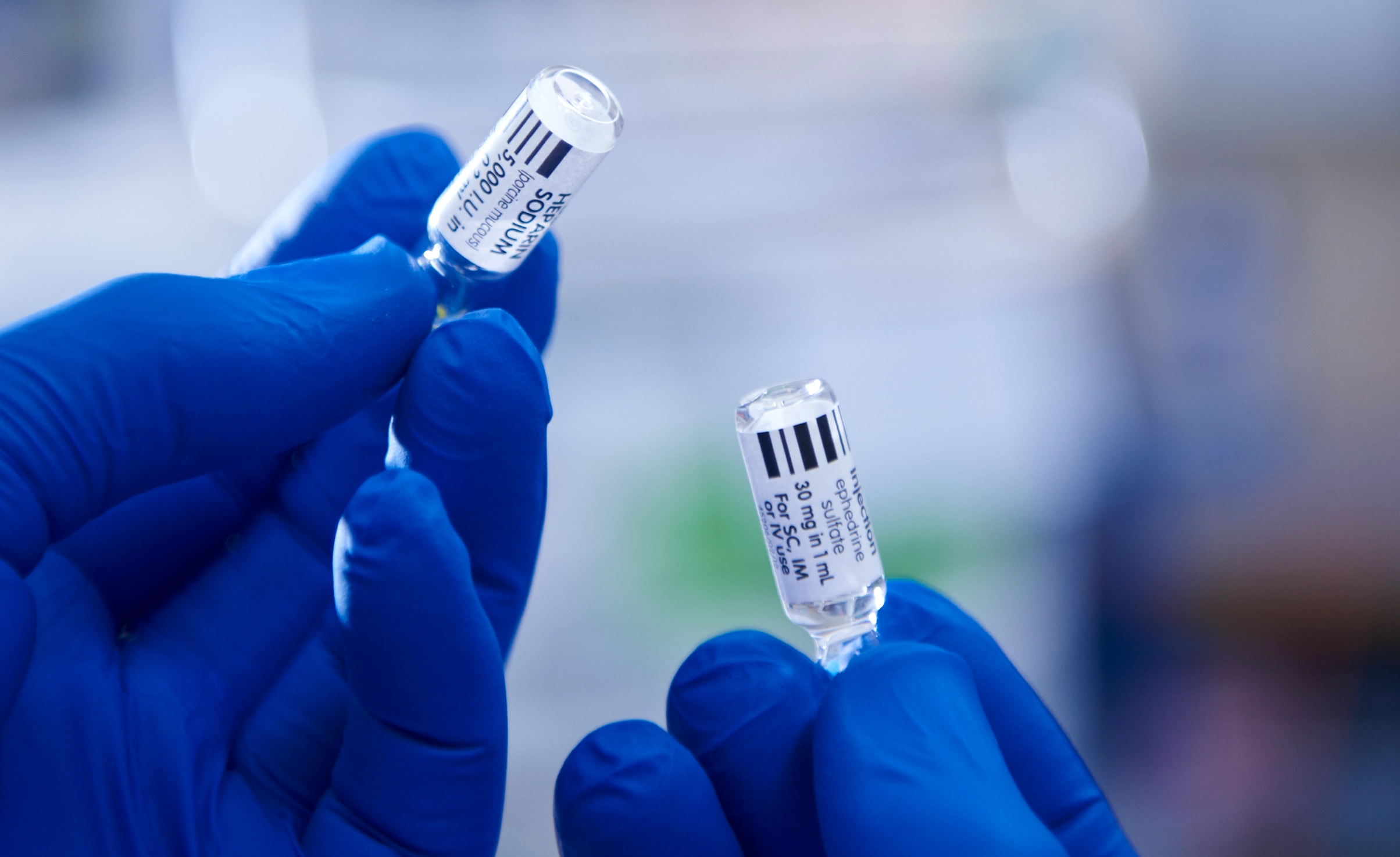 Gloved hands holding up two vials of medicine with writing on them