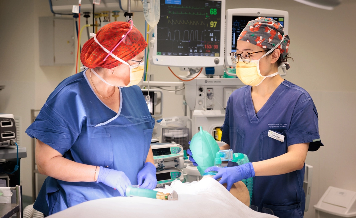 Two people in scrubs looking at each other while one uses a mask on a simulation patient