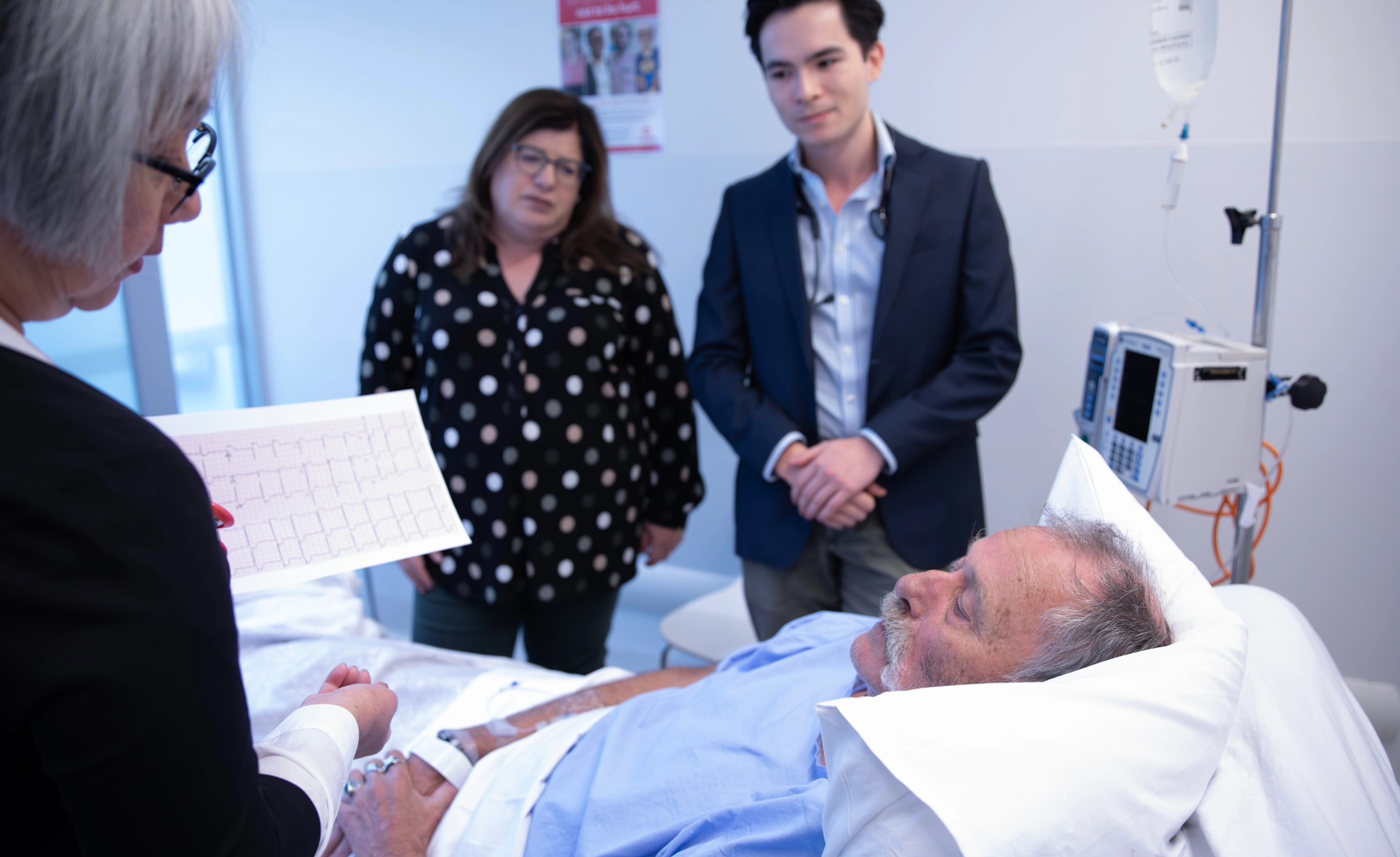 Three doctor's review an older male patient at a hospital bedside