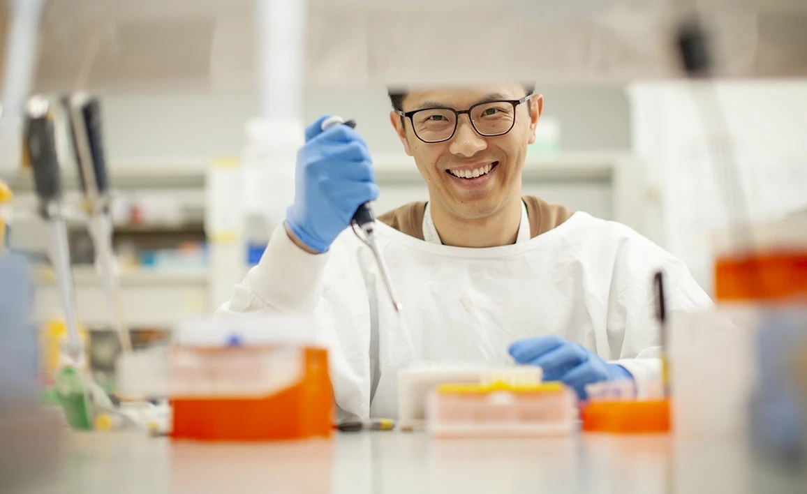 A researcher in a laboratory setting smiles while using a pipette, highlighting enthusiasm and innovation in scientific research.