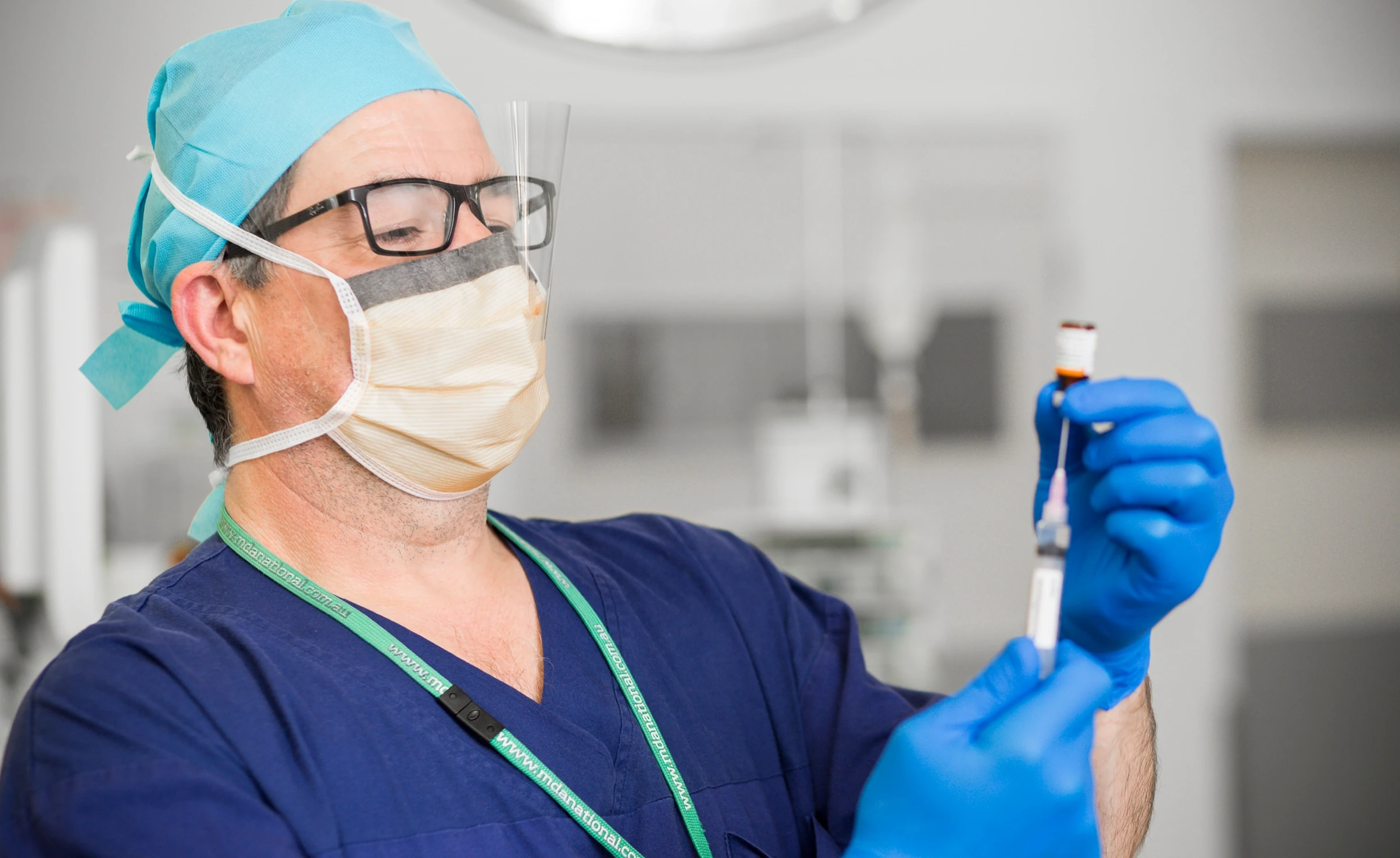 Doctor in scrubs and face mask with glasses drawing up needle of medicine