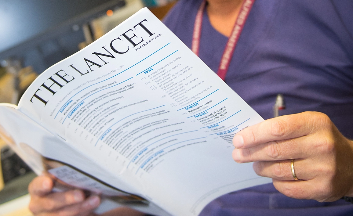 An anaesthetist in medical attire reading The Lancet, a well-known medical journal, reviewing published trial results