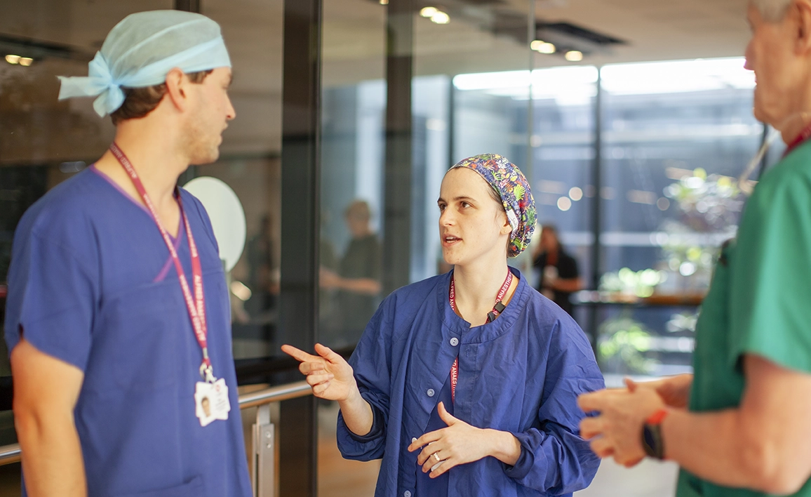 Three healthcare professionals in scrubs having a discussion in a hospital setting.