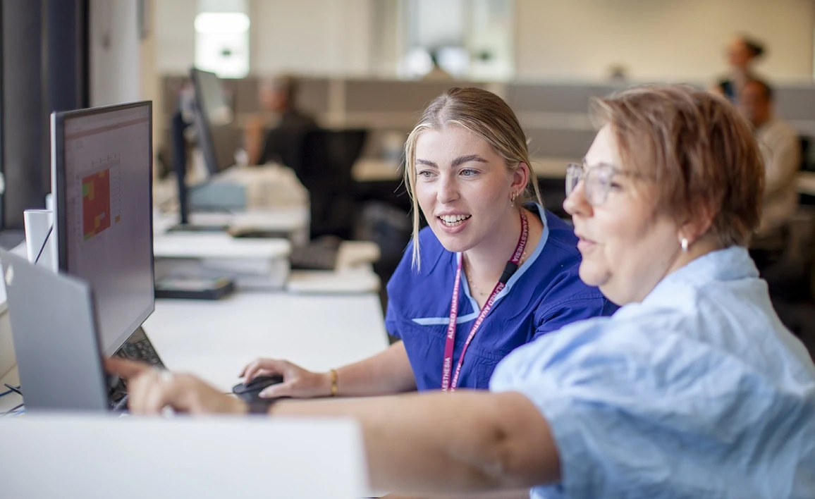 Two research coordinators collaborate at a computer, discussing data analysis and project management in a clinical research setting.